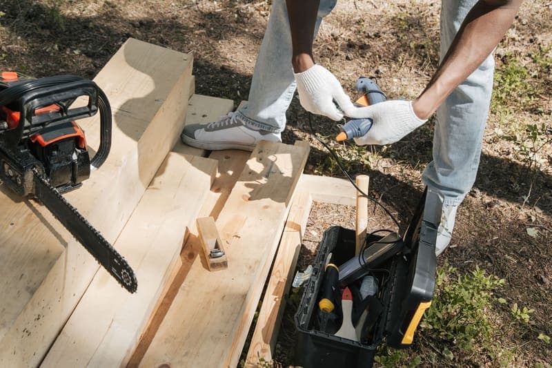 A carpenter working on a wooden panel with hand and power tools laid out beside it