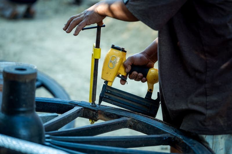 A worker holding a pneumatic nail gun against a wooden assembly
