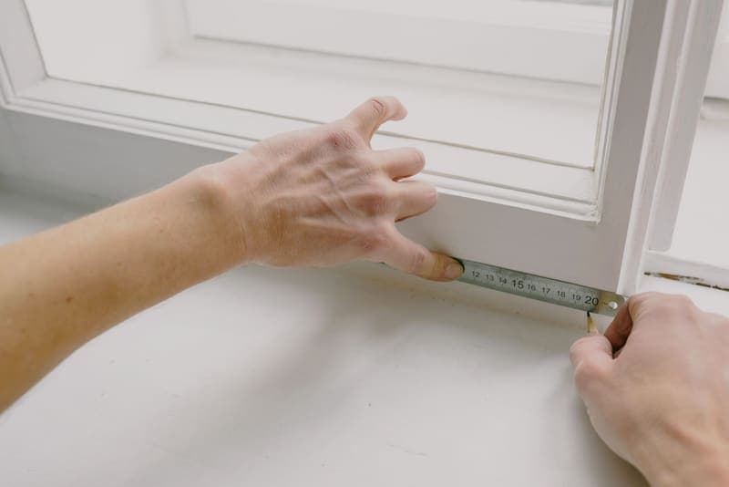 A worker measuring a wooden window frame with a ruler and pencil before fastening it