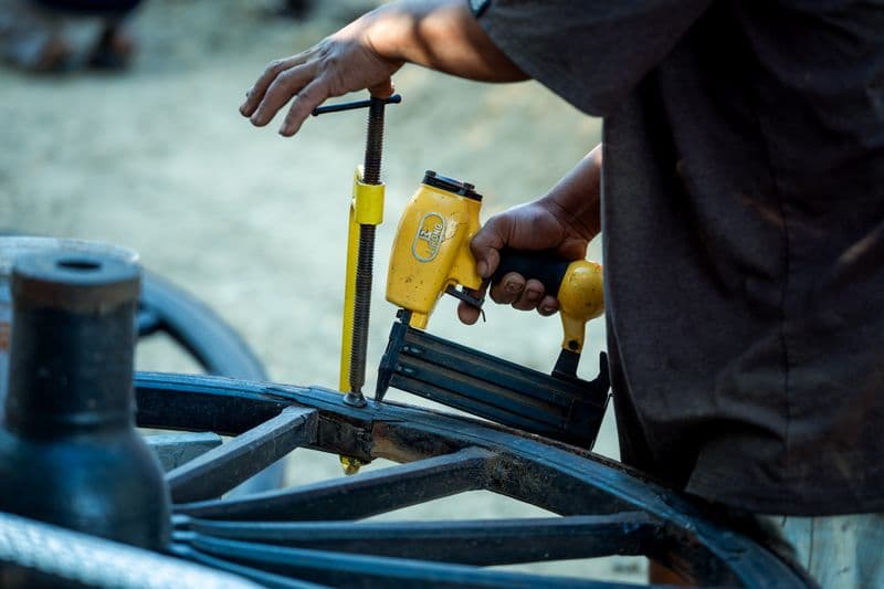 A worker using a pneumatic nail gun on a heavy wooden assembly