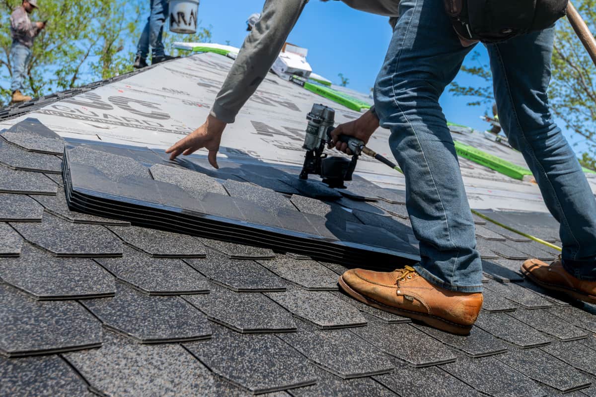 A roofer fastening shingles on a sloped roof deck